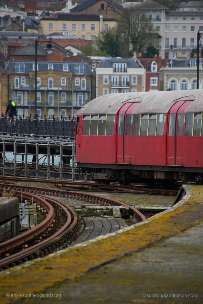 IOW Island Line - Exiting Ryde Pier Head Railway Station. In the background the city and between the train and the background the pedestrian bridge on the pier. Note the exposed power rail on the rarely used track on the left.